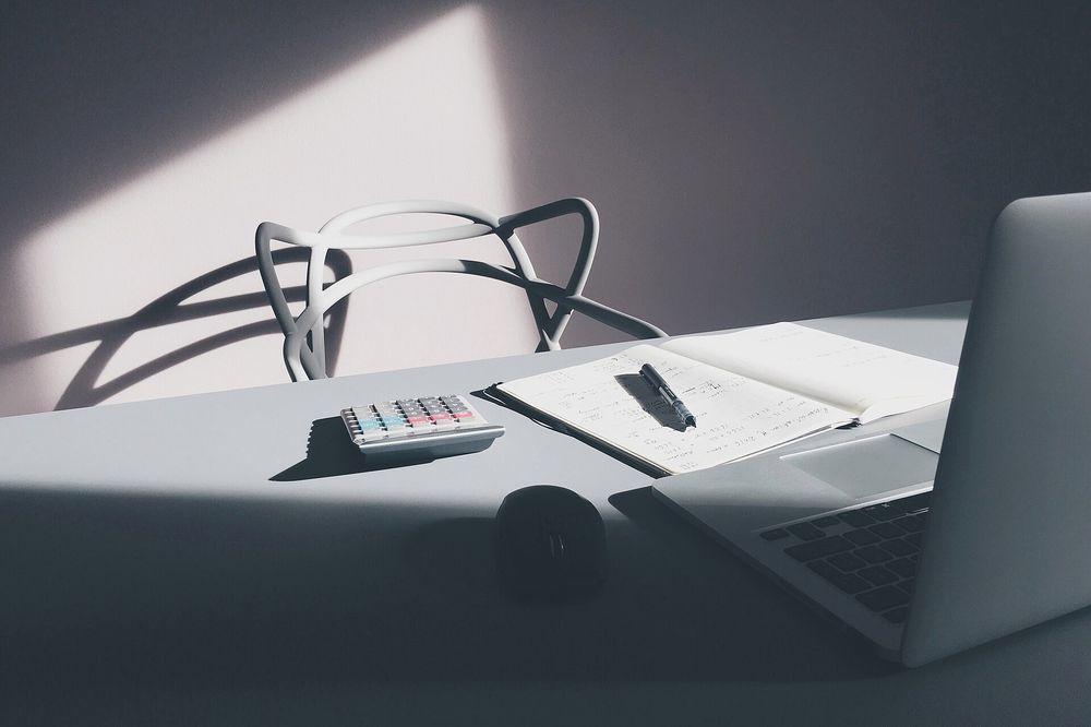 A desk with a calculator, notes and a laptop