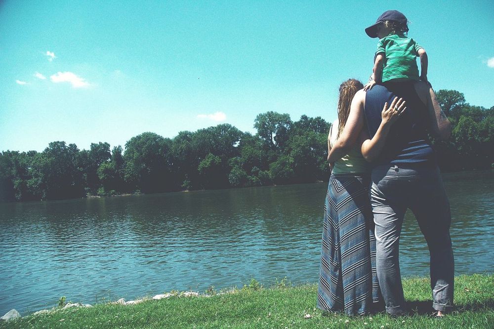 A family standing by a lake, seen from behind